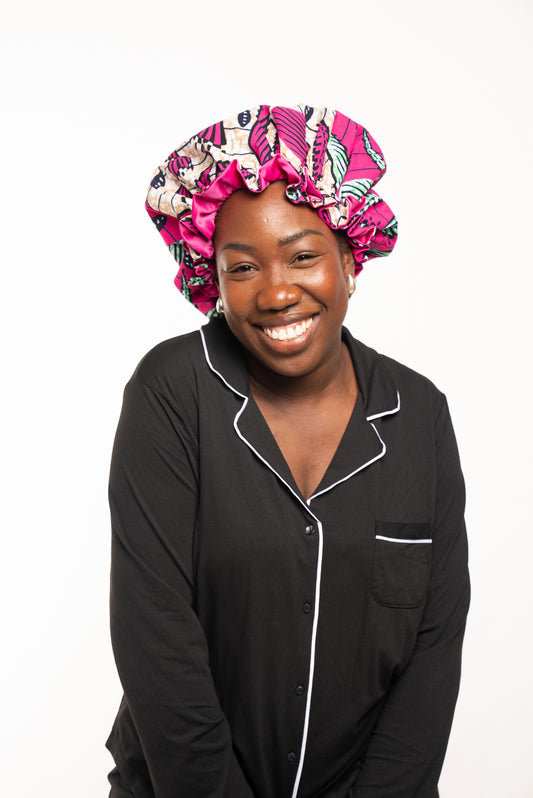 Black Woman smiling wearing a black pyjamas with pink silk hair bonnet 