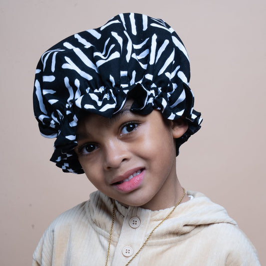 Child wearing a black and white patterned hair bonnet  against a plain background