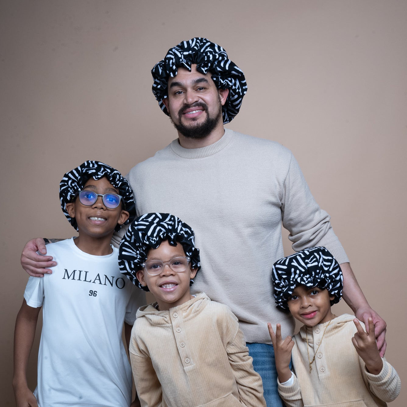 Man with three children wearing matching hair bonnets against a plain background