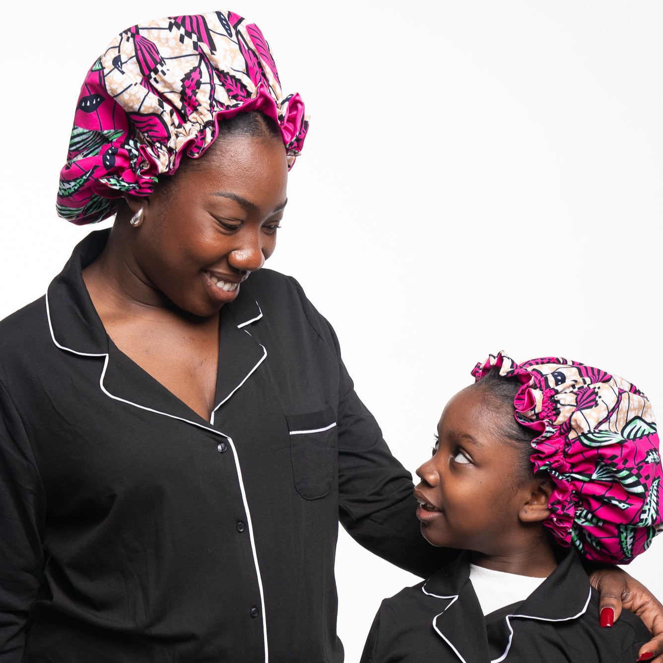 Woman and child wearing matching black outfits with pink bonnets on a white background